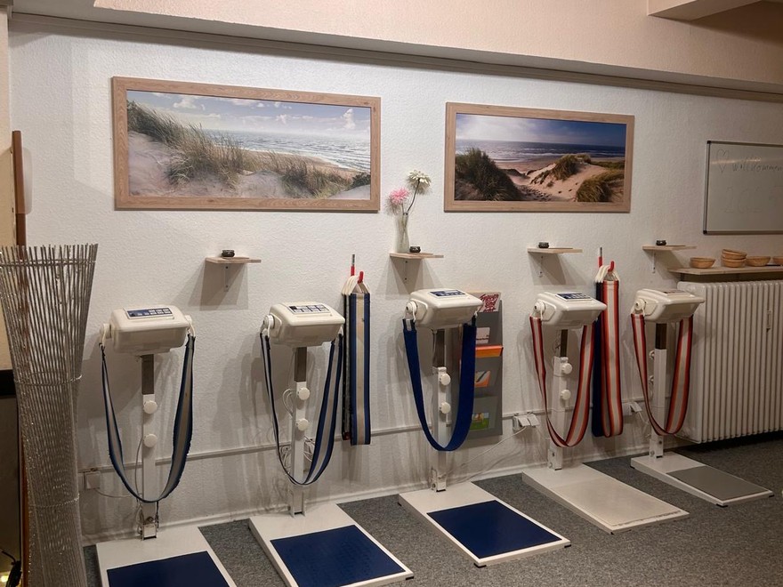 Fünf Bandmassagegeräte nebeneinander an der Wand, jedes mit einem breiten Band